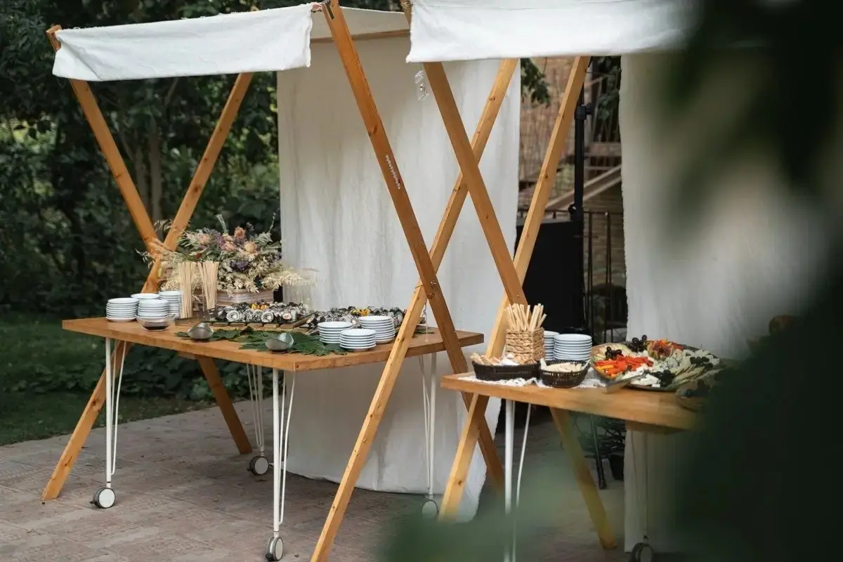 Un bufet en el jardín: mesa de madera con platos, cestas y fuentes bajo un toldo blanco