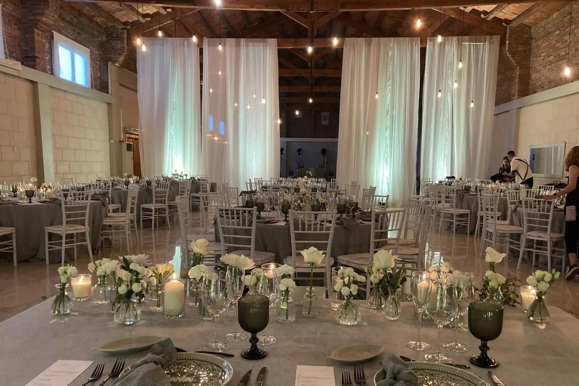 El salón con cortinas blancas colgadas del techo, mesas con flores blancas y velas, y sillas de resina blancas