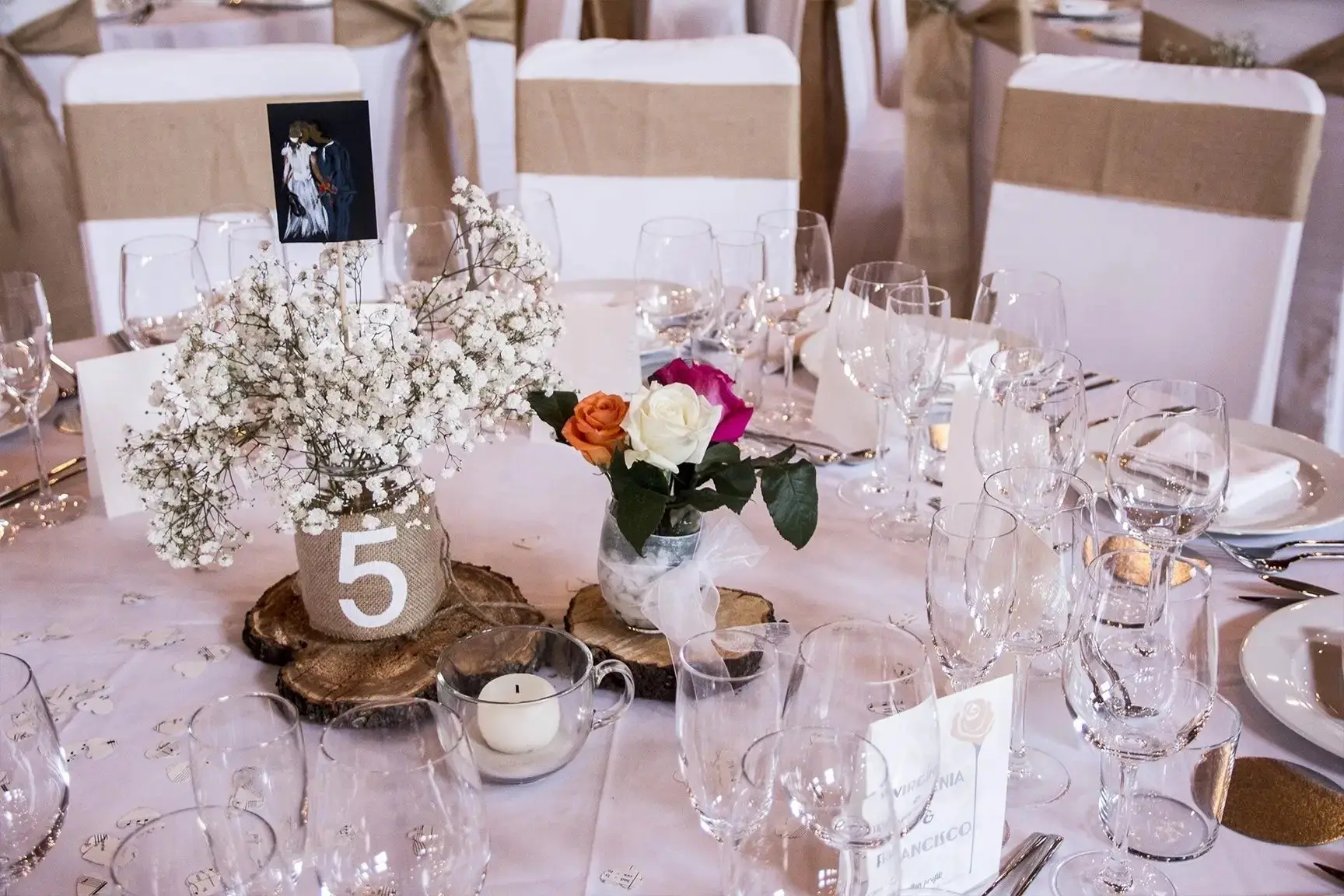 Un centro de mesa con gipsófila y rosas naranja, blancas y fucsia, sobre un tronco con el número 5